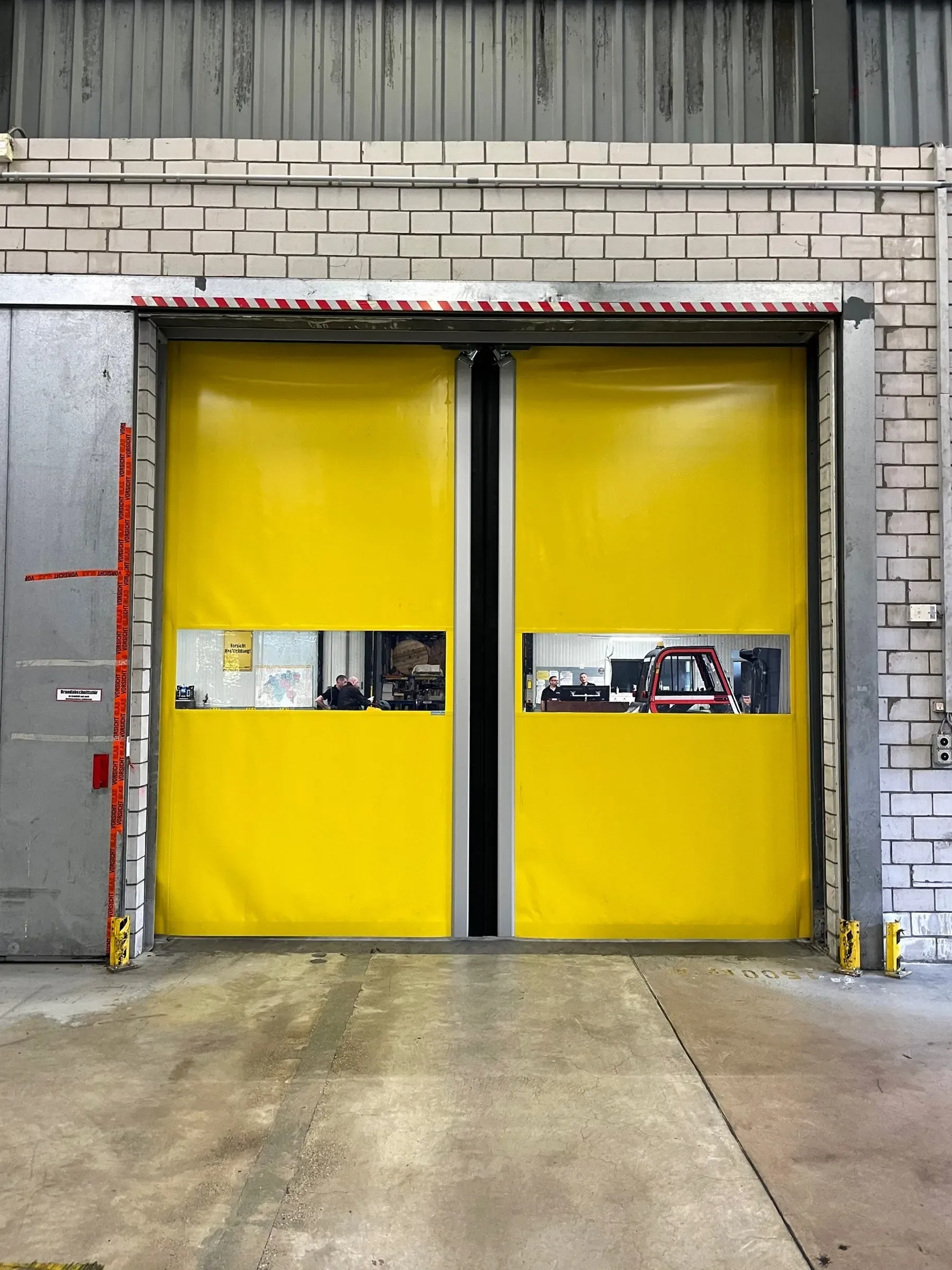 Geschlossenes seitlich öffnendes Schnelllauftor mit gelbem Torbehang und Sichtfenstern auf einem Logistikareal in Rümlang, dahinter ein Stapler